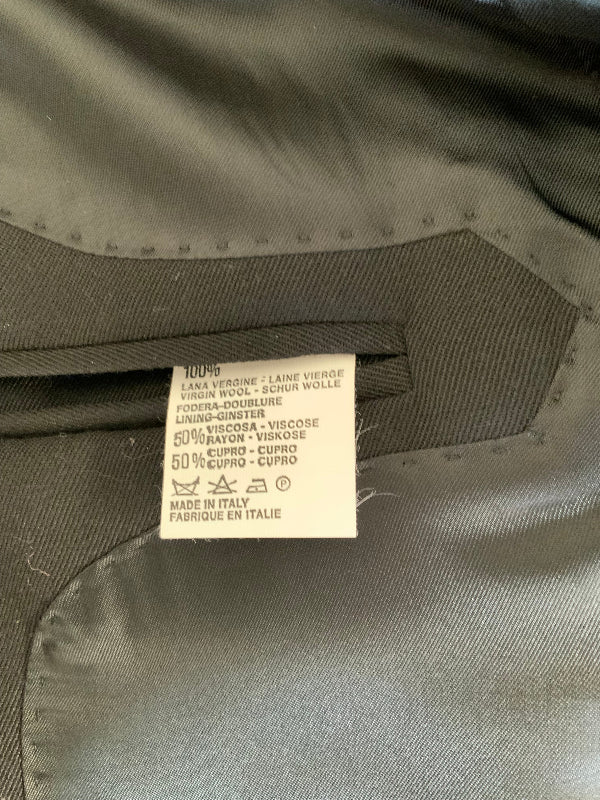Close-up of a garment's interior label sewn onto dark gray fabric, showing care instructions and a small circular logo.