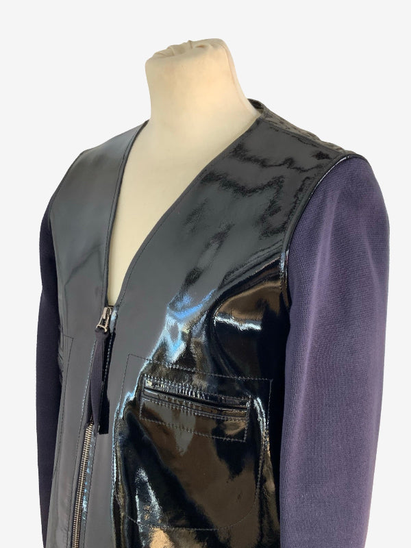A cotton knitted sleeve jacket with a glossy black patent leather front panel and a matte dark gray side panel, styled over a purple long-sleeve shirt on a mannequin torso against a white background.