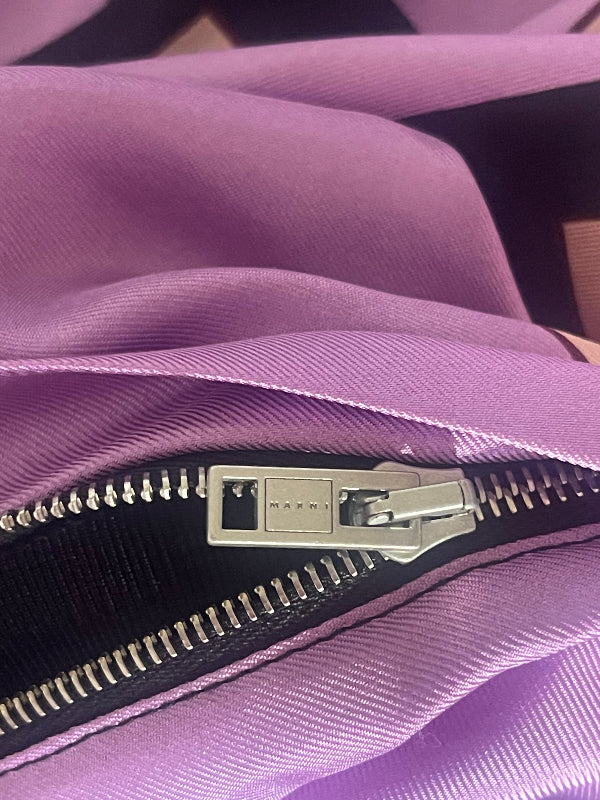 Close-up of a purple fabric zipper with a silver metal pull tab on a black zipper track.