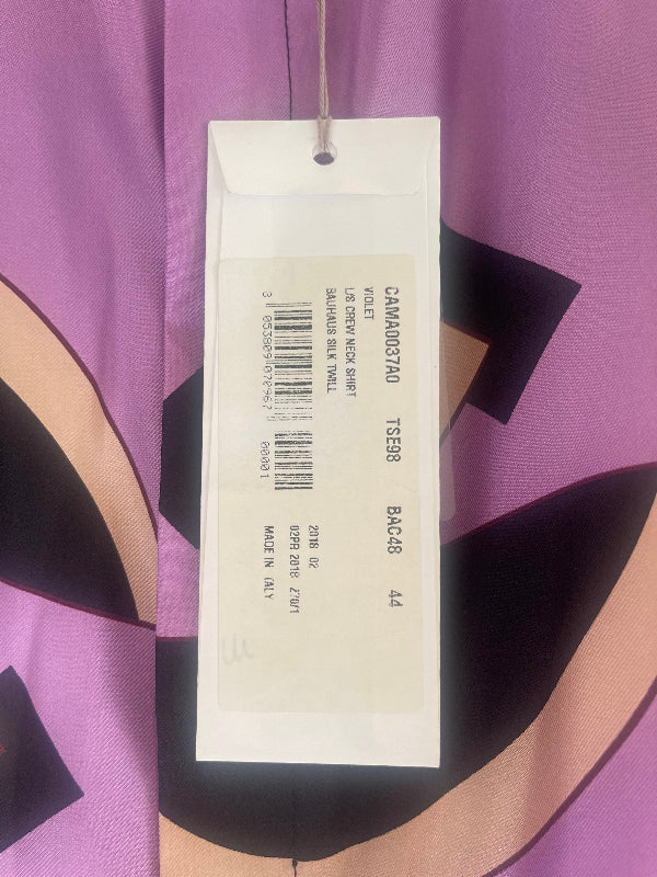 A white garment hangtag with printed text and a barcode attached to a purple patterned fabric garment.