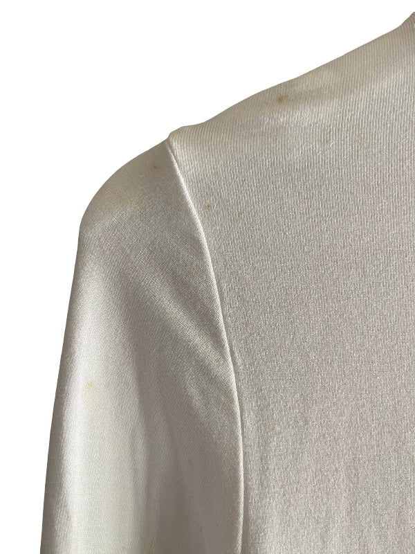 Close-up of a white knit fabric garment, showing the texture, slight faint marks and shoulder seam against a plain white background.