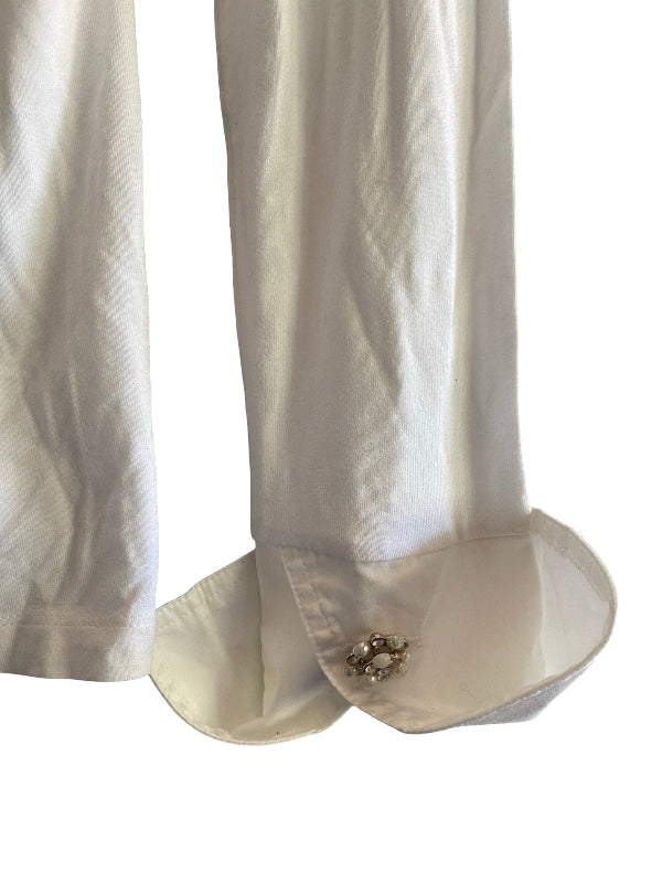 Close-up of a white or off-white fabric garment with a decorative jeweled button detail on the cuff, shown against a plain white background.