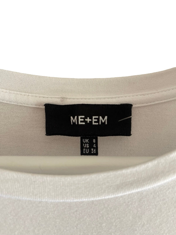 Close-up of the inside collar of a light cream/off-white t-shirt, showing a black brand label that reads 'ME+EM' with size information below it.