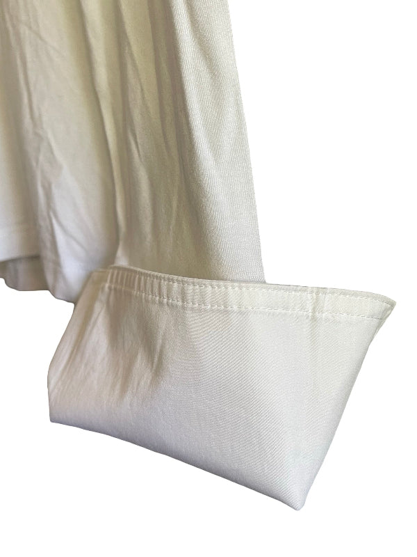 A close-up of a light cream or off-white fabric garment, showing a folded cuff with neat stitching against a plain white background.