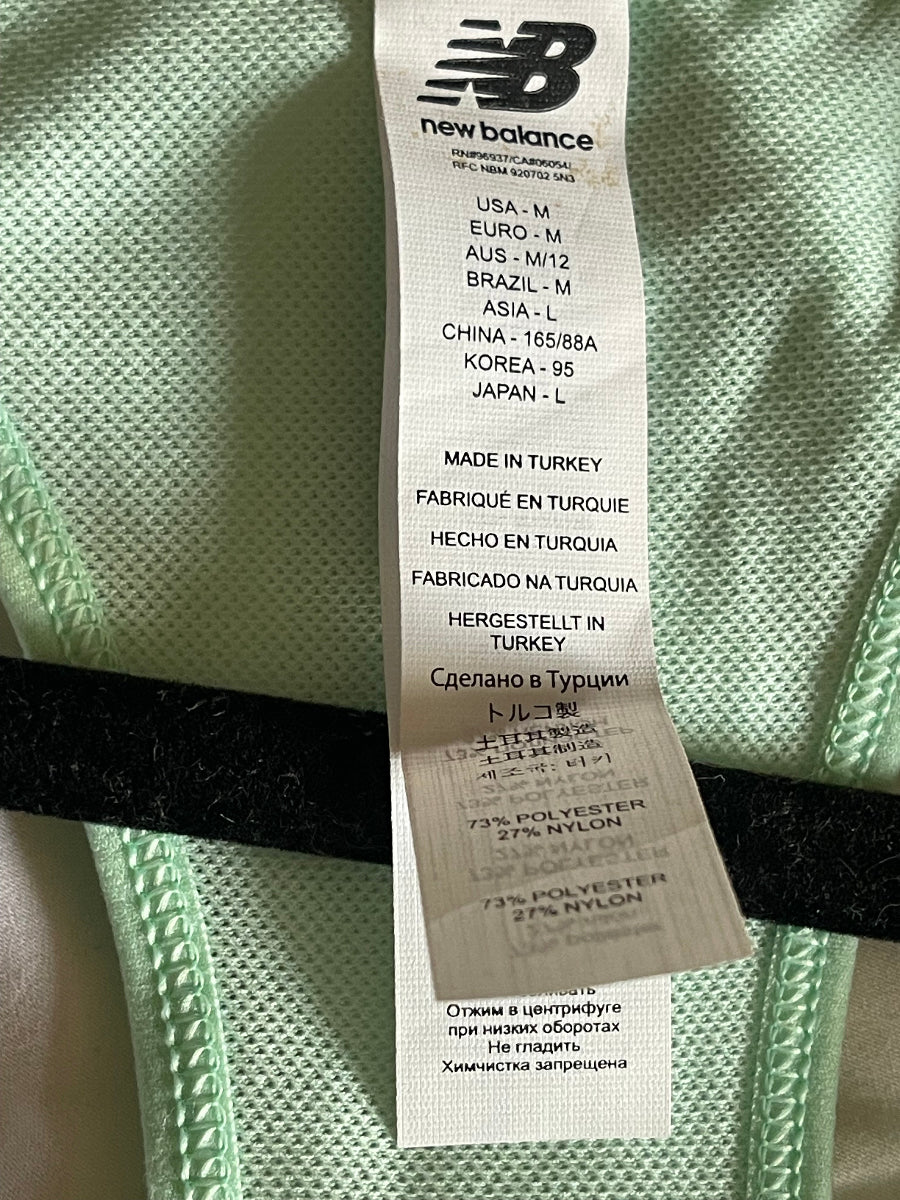 Close-up of a New Balance garment label sewn onto mint green athletic mesh fabric.