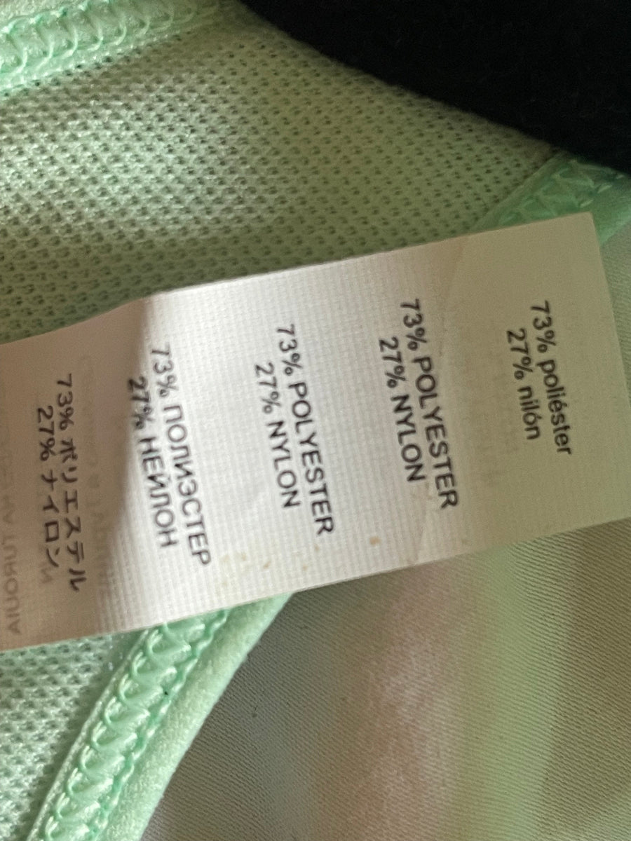 A close-up of a garment's interior label showing fabric composition: 73% polyester and 27% nylon, with pale mint green mesh fabric visible around the tag.