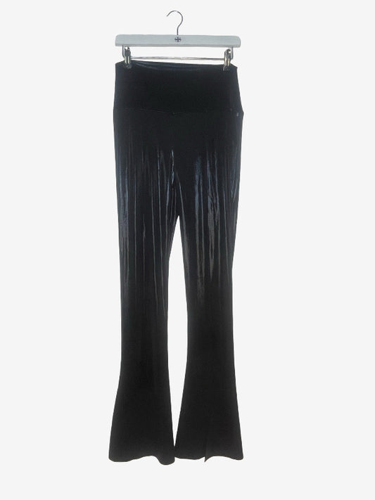 Black flared pleated pants hanging from a white hanger against a light gray background.