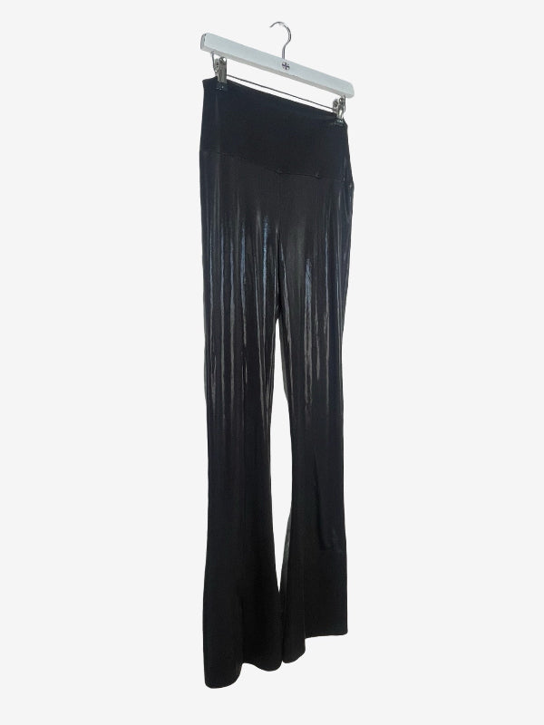Black pleated flare pants hanging from a white plastic hanger against a light gray background.