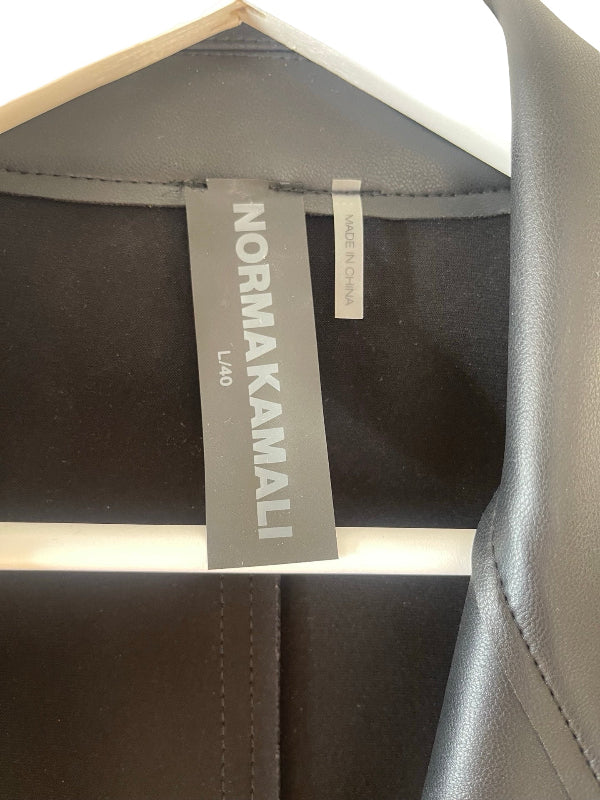 Close-up of a garment hanging on a white hanger, showing a dark gray interior label that reads NORMA Kamali and L40, alongside a small white tag.