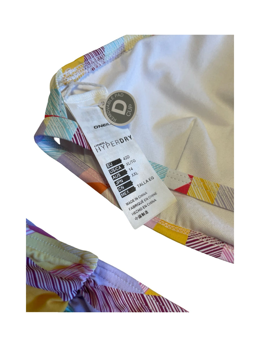 Close-up of a garment's inner waistband showing a colorful striped elastic trim, a white inner lining, and a hangtag with size information. The tag reads 'DYNAMIC Hyperday' and shows sizing for sizes 12 to 24.