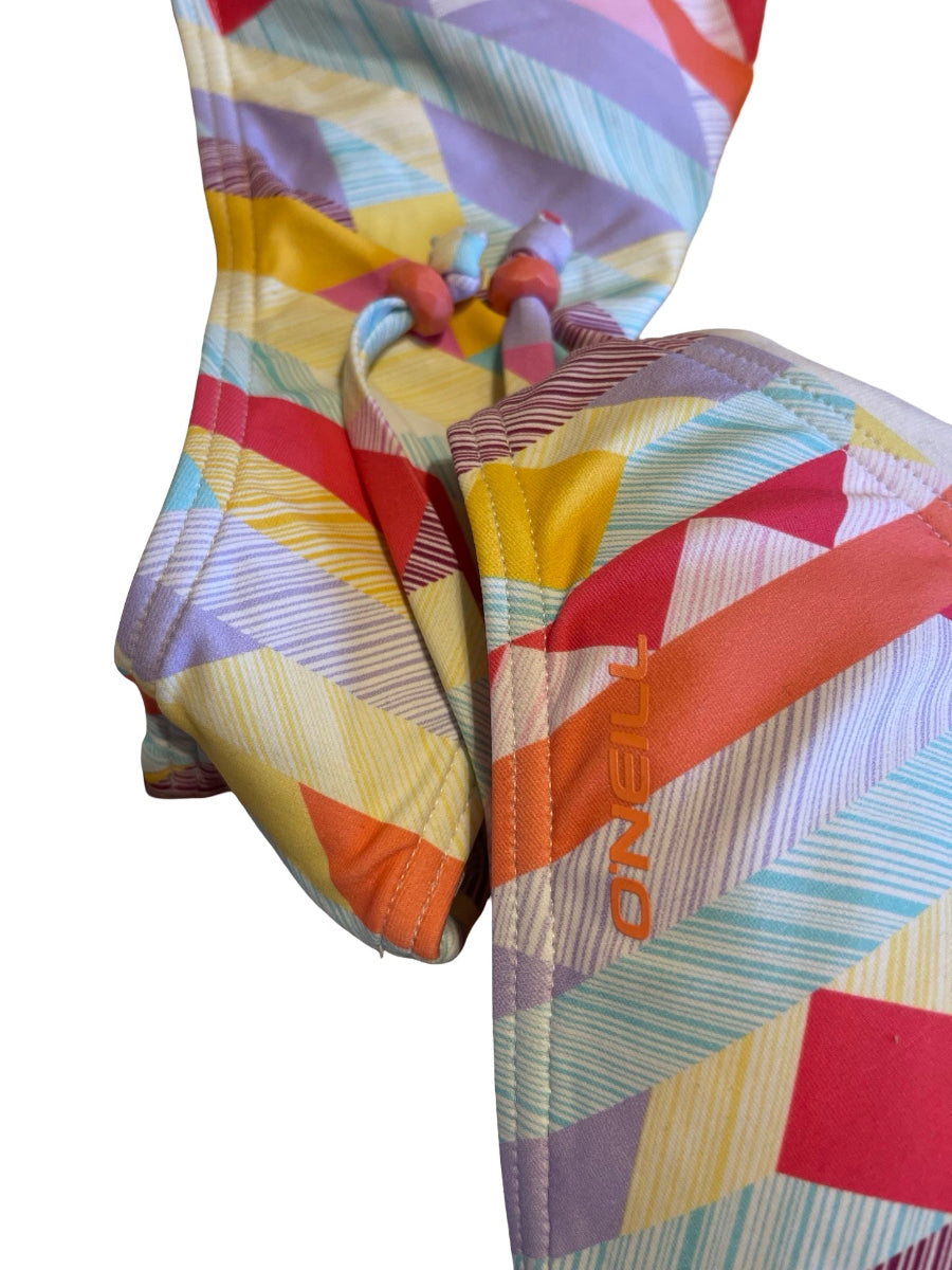 Close-up of a colorful patterned garment, likely a swimsuit or cover-up, showing a geometric print in yellow, orange, red, purple, and light blue with a drawstring closure. The brand name 'TUNISO' is visible in orange on the fabric.