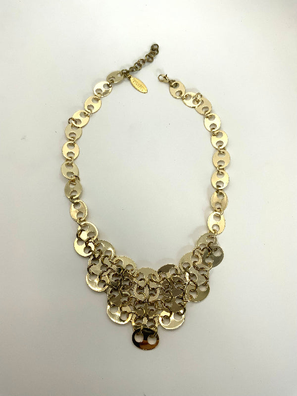 A gold-toned statement necklace featuring a layered chain design with circular disc links and a small charm at the center, displayed on a plain white background.