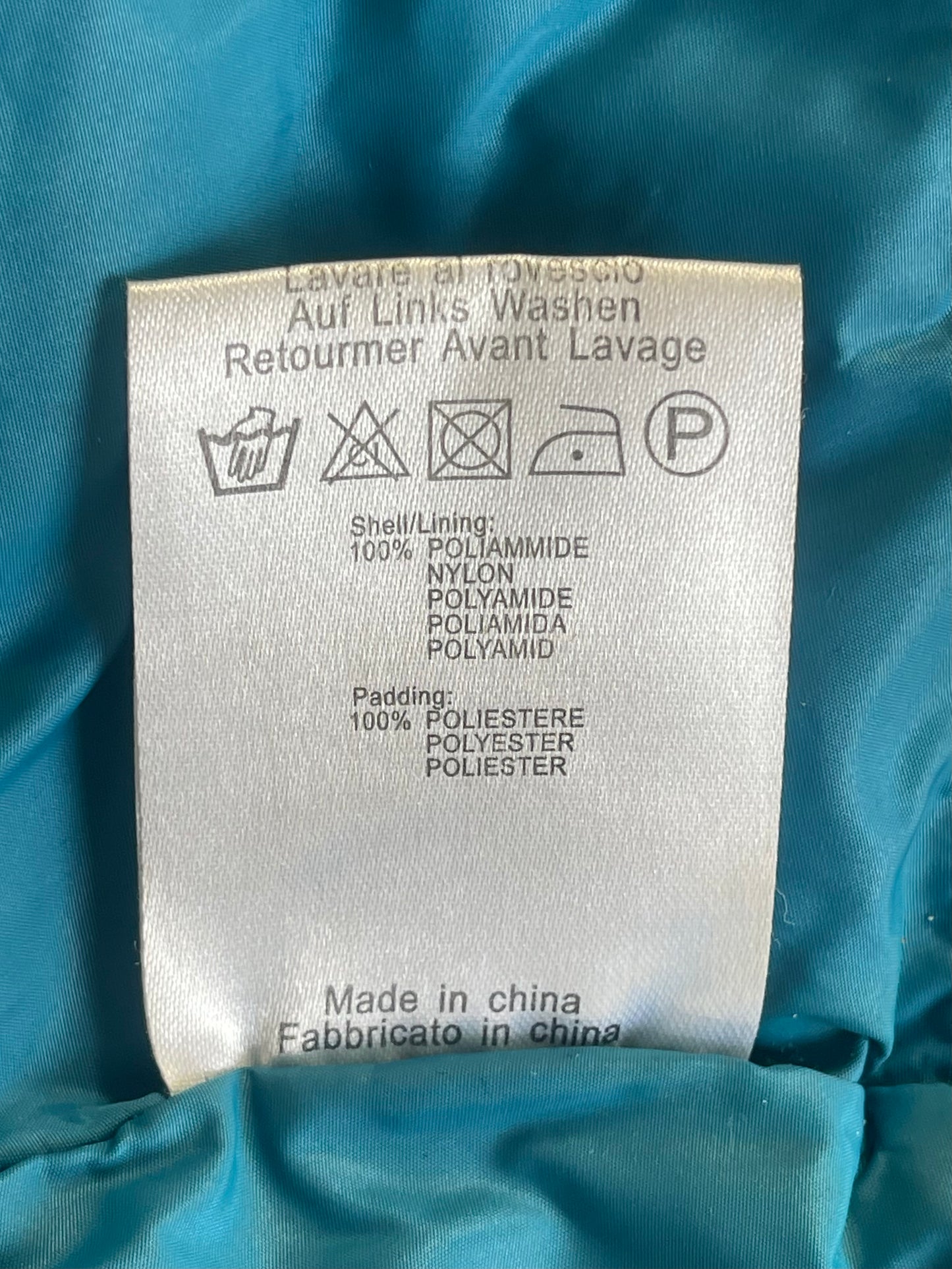 A close-up of a white garment care label sewn onto shiny teal fabric, showing washing instructions and material composition.