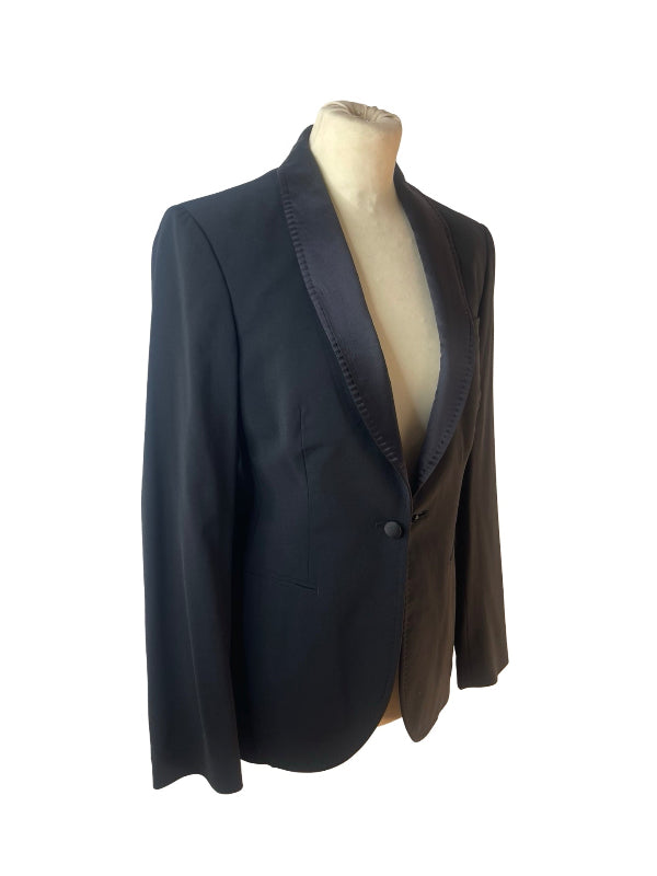 A black tailored blazer with satin peak lapels, displayed on a beige mannequin torso against a plain white background.