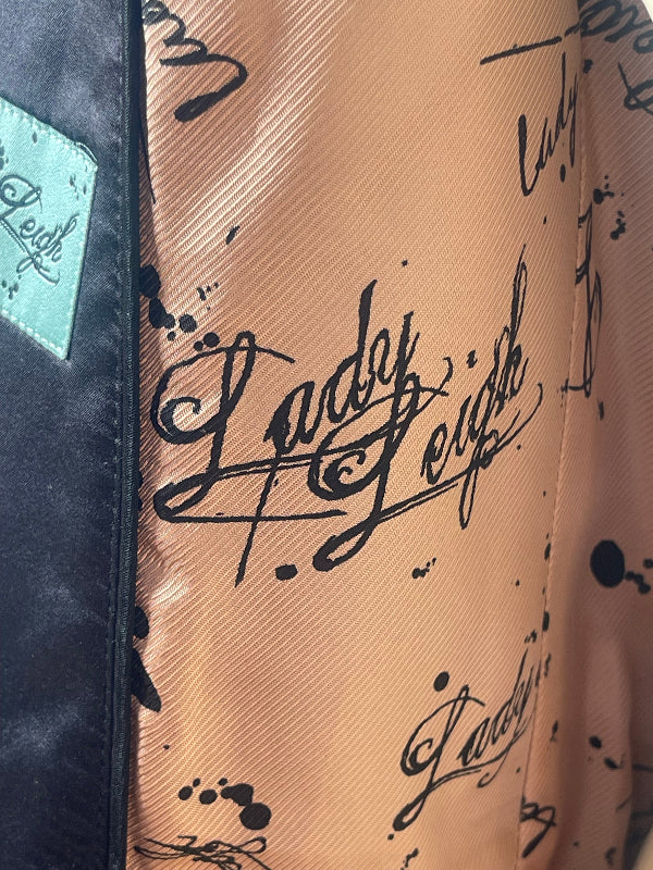 Close-up of a garment featuring a peach-colored satin-like panel printed with black cursive 'Lady Gaga' script and black paint splatters, next to a black fabric section with a light blue patch labeled 'Lady Gaga'.