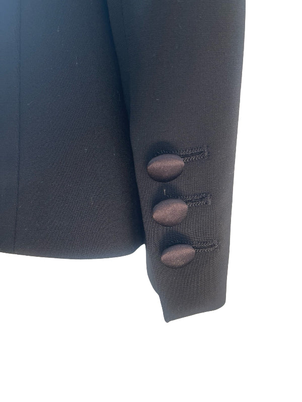 Close-up of black blazer sleeve showing three decorative oval buttons with stitched details on the cuff, set against a plain white background.
