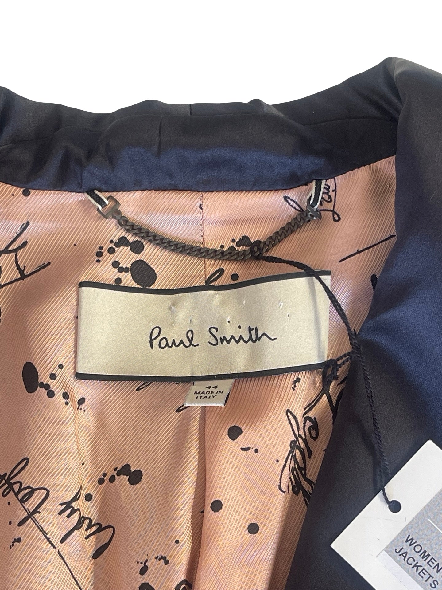 Close-up of a Paul Smith women's jacket interior showing a peach-colored printed lining with black script and splatter motifs, a cream brand label, and a black outer fabric.