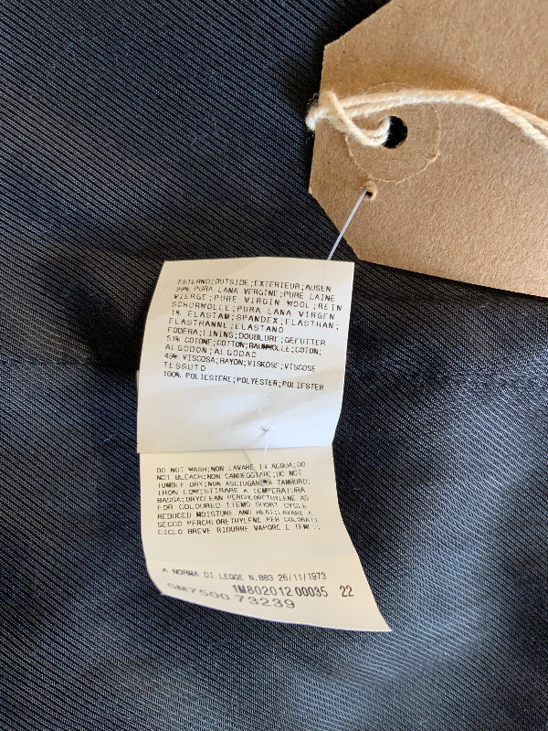 A close-up of a folded white paper garment tag attached to a brown kraft paper hangtag with string, placed on black textured fabric.