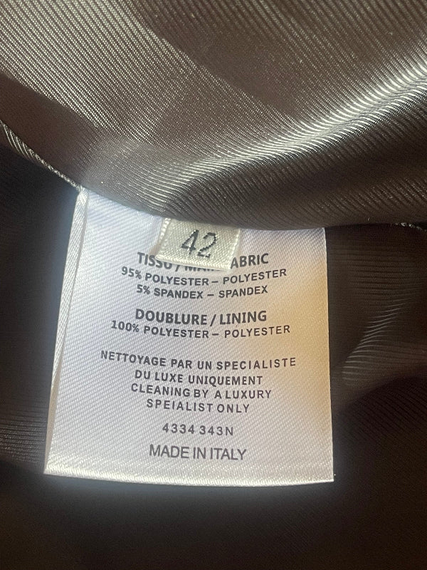 A close-up of a sewn-in fabric tag showing material details, placed on dark gray or black textured fabric.