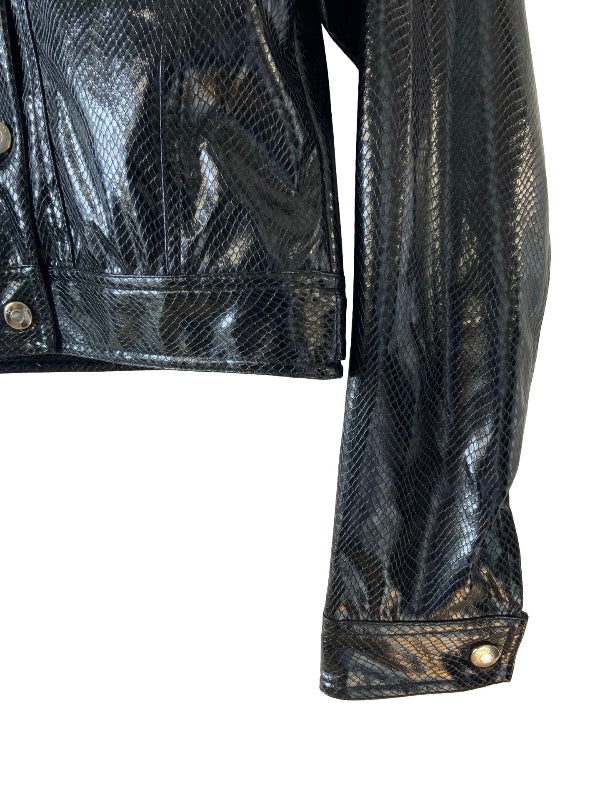 Close-up of a black snakeskin-patterned jacket with a glossy finish, featuring a button, a sleeve with a cuff, and silver-tone snap buttons, shown against a plain white background.