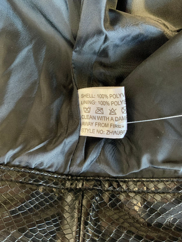 Close-up of a garment's interior label sewn onto shiny black  lining, with part of a metallic snakeskin-patterned exterior visible below.