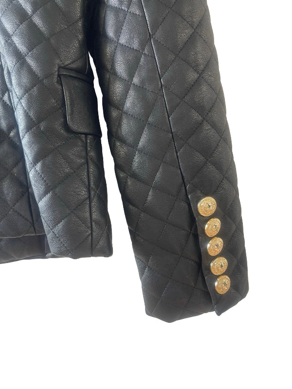 Close-up of a black quilted faux leather  jacket sleeve with five gold buttons on the cuff, shown against a plain white background.