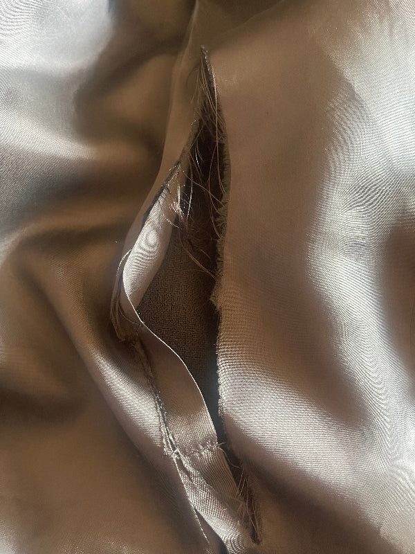 A close-up of a black -colored satin or silk fabric with a visible frayed tear or cut showing a darker inner Jacket