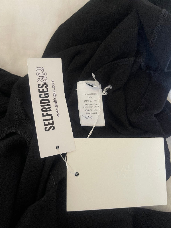 A close-up of black clothing with attached white retail tags, including a prominent tag reading SELF RIDGES & CO.