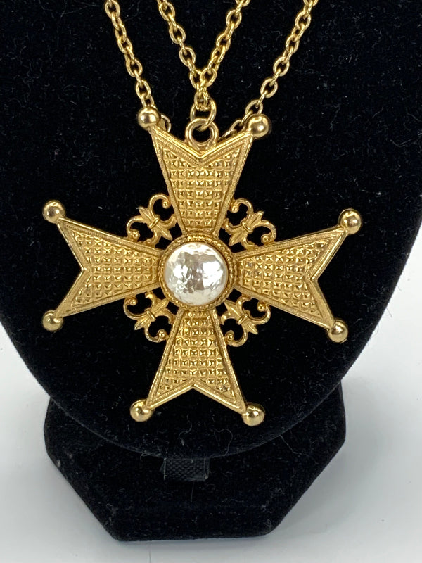 A gold-toned cross pendant necklace with a textured, beaded star design and a central clear rhinestone, displayed on a black velvet jewelry bust.