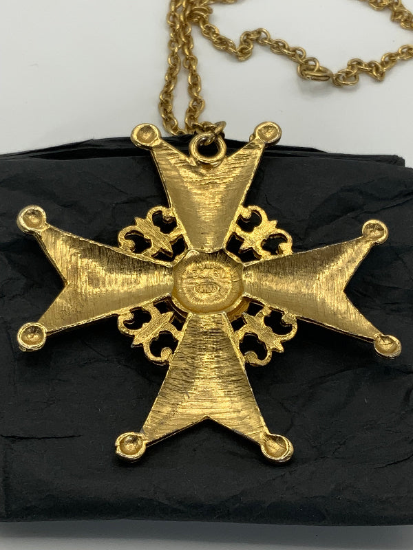 A gold-toned medieval-style cross pendant necklace with a textured finish, hanging from a gold chain against a black textured background.