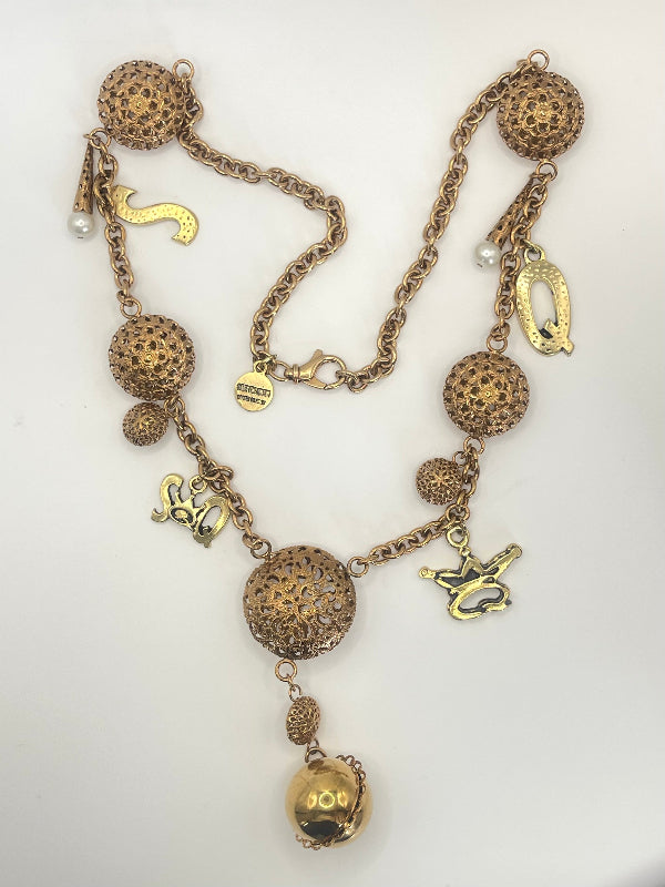 A vintage-style gold-tone necklace featuring textured spherical beads, a central hanging ball charm, and several dangling animal and abstract charms on a chain, displayed on a plain white background.
