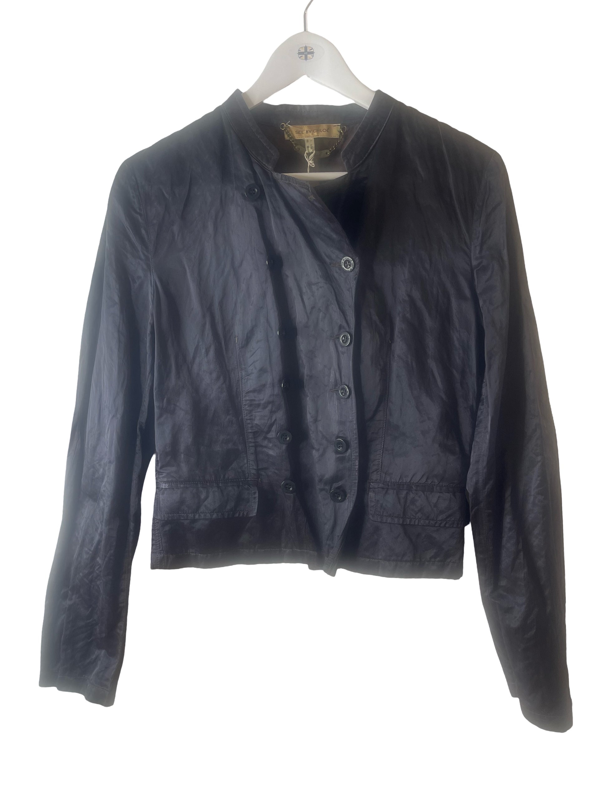 A black cropped jacket with a button-front closure and long sleeves, hanging on a white hanger against a plain white background.