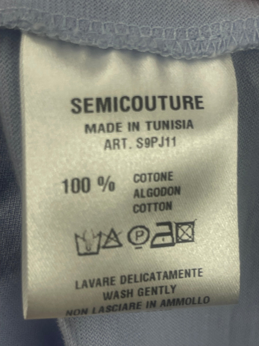 Close-up of a garment's interior fabric label reading 'SEMICOUTURE', 'MADE IN TUNISIA', 'ART. S9PJ11', '100% COTONE ALGODON COTTON', with care symbols and washing instructions in Italian.