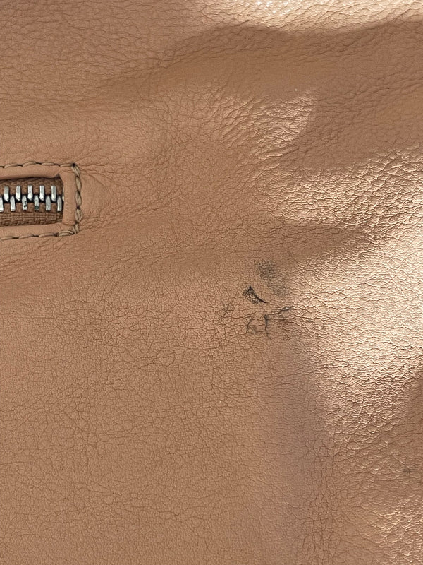 Close-up of a beige textured leather surface with a zipper and a small dark scratch or mark near the center.