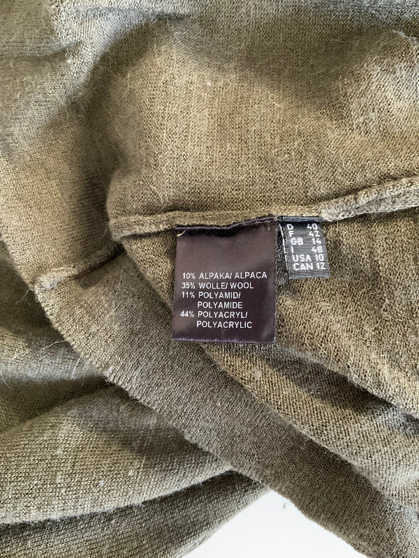 Close-up of a folded olive green fabric garment showing a sewn-in size and material label. The label reads 100% Alpaca Alpaca, 35% Wool, 11% Polyamide, 44% Polyacrylic, and shows size D 43-46 USA 10 CAN 12.
