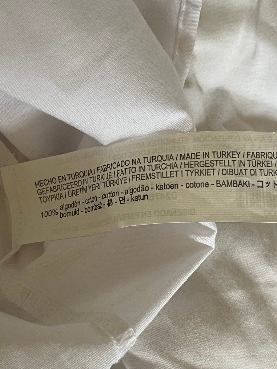 A close-up of a sewn-on product label attached to white fabric, showing text including '100% bombo cotton' and 'Made in Turkey'.