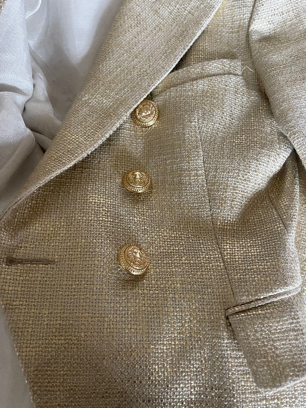 Close-up of a textured beige or champagne-colored fabric garment with three decorative gold buttons, laid over white fabric.