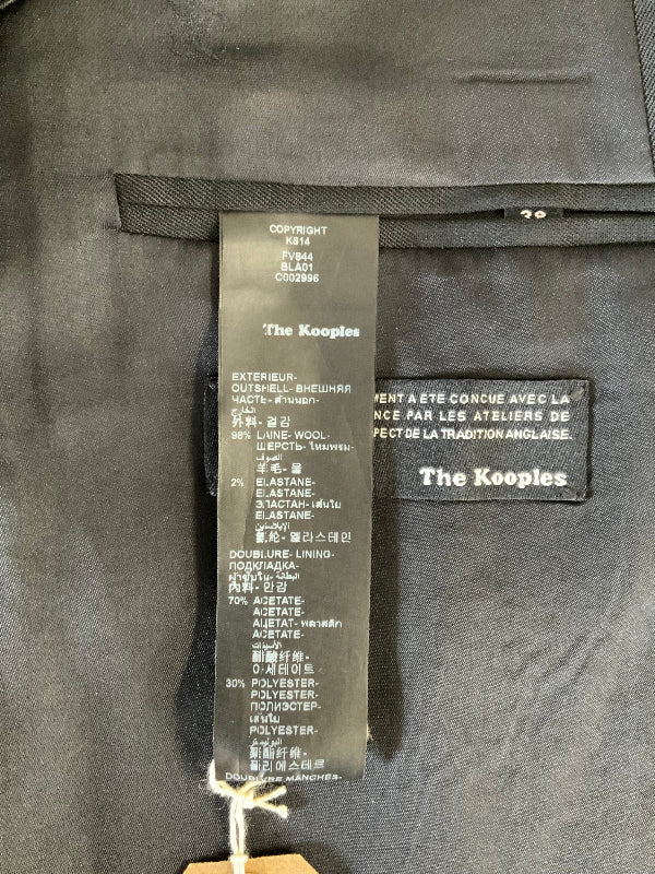 Close-up of a black garment interior showing a black fabric tag labeled 'The Kooples' and a black sewn-in brand patch with the same logo.