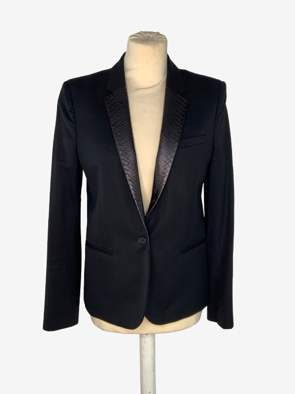 A black single-breasted blazer with textured patterned lapels, displayed on a cream-colored mannequin torso against a light gray background.