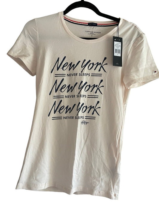 A blush-colored short-sleeve t-shirt with a black graphic print reading 'New York Never Sleeps' hanging on a black hanger against a white background.