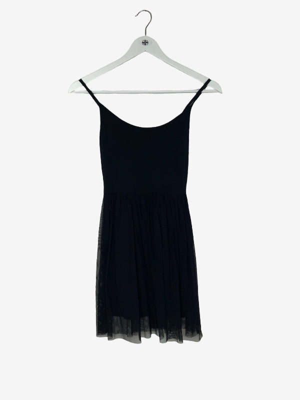 A black spaghetti-strap mini dress with a sheer tulle hem, hanging on a white plastic hanger against a light gray background.