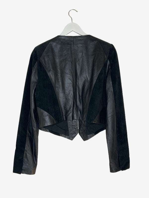 Black asymmetrical jacket with mixed leather and suede panels, hanging on a white hanger against a light gray background.