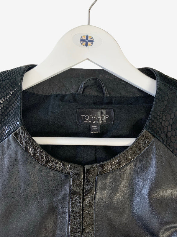 A close-up of a black leather jacket with textured snakeskin-patterned shoulder panels, hanging on a white hanger with a TOPSHOP label visible.