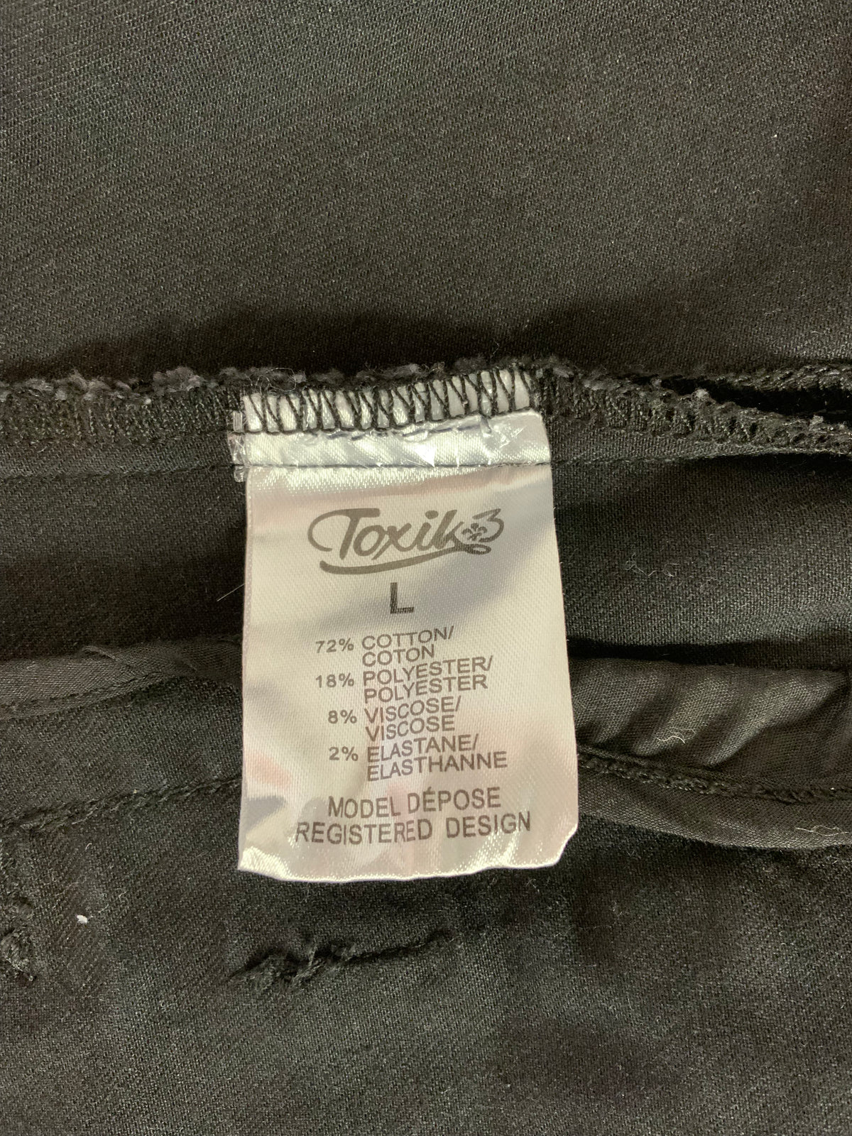 Close-up of a sewn-in size label reading ToxiK's on washed black denim fabric.
