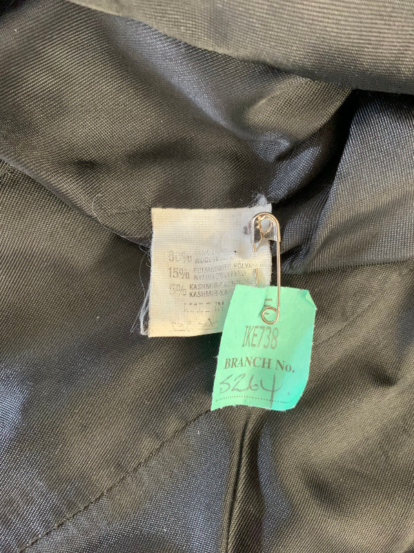 Close-up of a black garment interior showing a sewn-in label and a bright green dry cleaning branch tag attached with a safety pin.