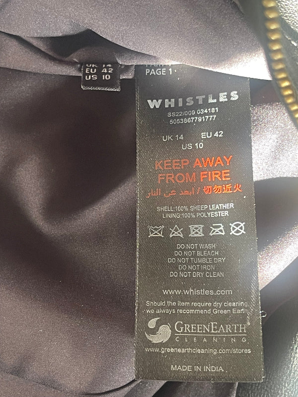 A close-up of a black garment label with care instructions and branding. The label reads Whistles and includes a Green Earth Cleaning logo and 'Made in India' text, photographed against dark fabric.