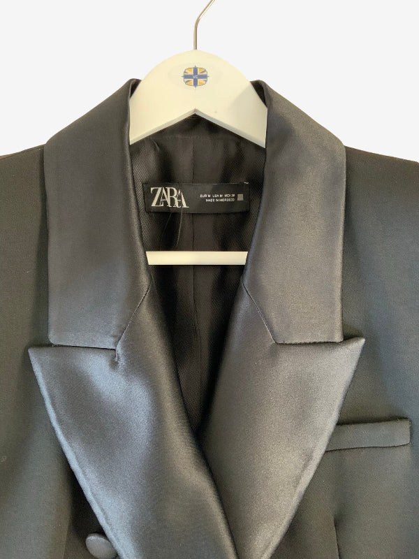 A close-up of a black satin lapel dinner  jacket hanging on a white hanger with a visible Zara label.
