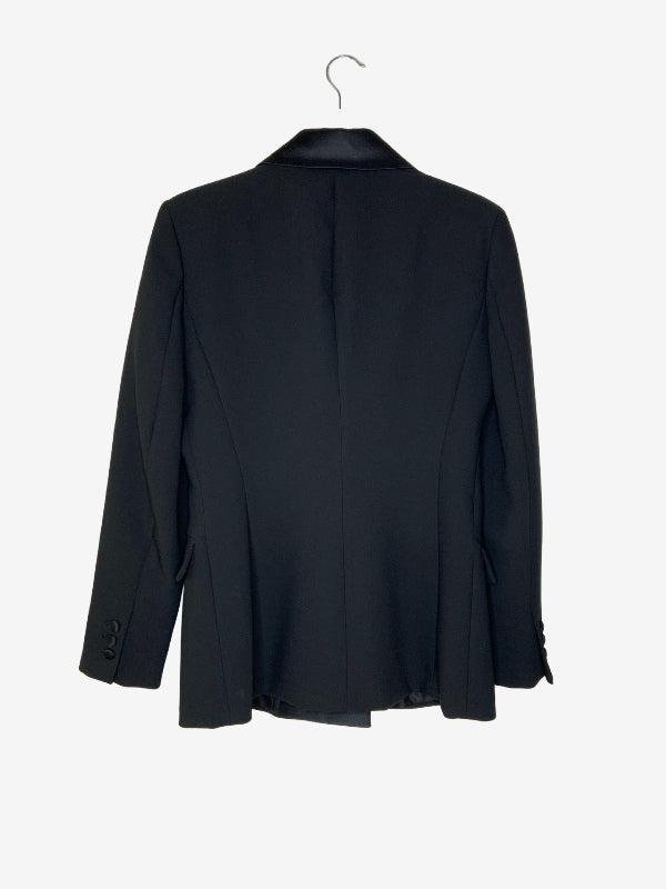 A black tailored blazer jacket hanging on a metal hanger against a plain light gray background, shown from the back.