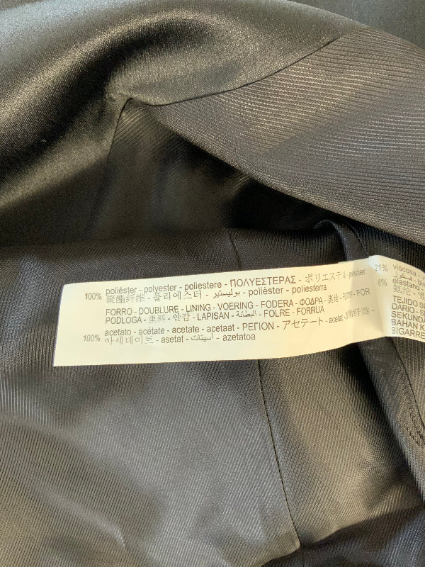 Close-up of a garment's interior collar area showing a white fabric care label with multilingual text, set against dark gray satin-like fabric.
