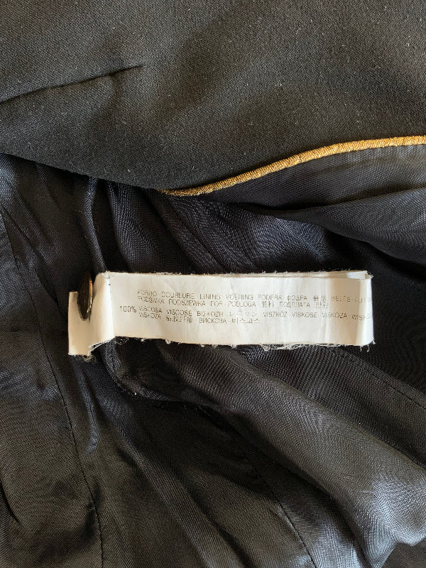 Close-up of the inside content label of a black coat or jacket, showing a white sewn-in size and care label attached to the collar, with a thin gold trim line visible above it.